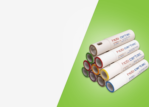 Uma pilha de rolos cerâmicos industriais brancos da marca Hob Certec, organizados em formato de pirâmide sobre um fundo verde.